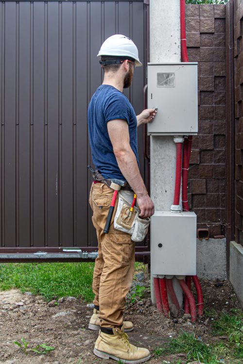 Electrician builder at work, examines the cable connection in the electrical line in the fuselage of an industrial switchboard. Professional in overalls with an electrician's tool.